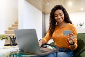 Happy woman holding debit credit card, using pc